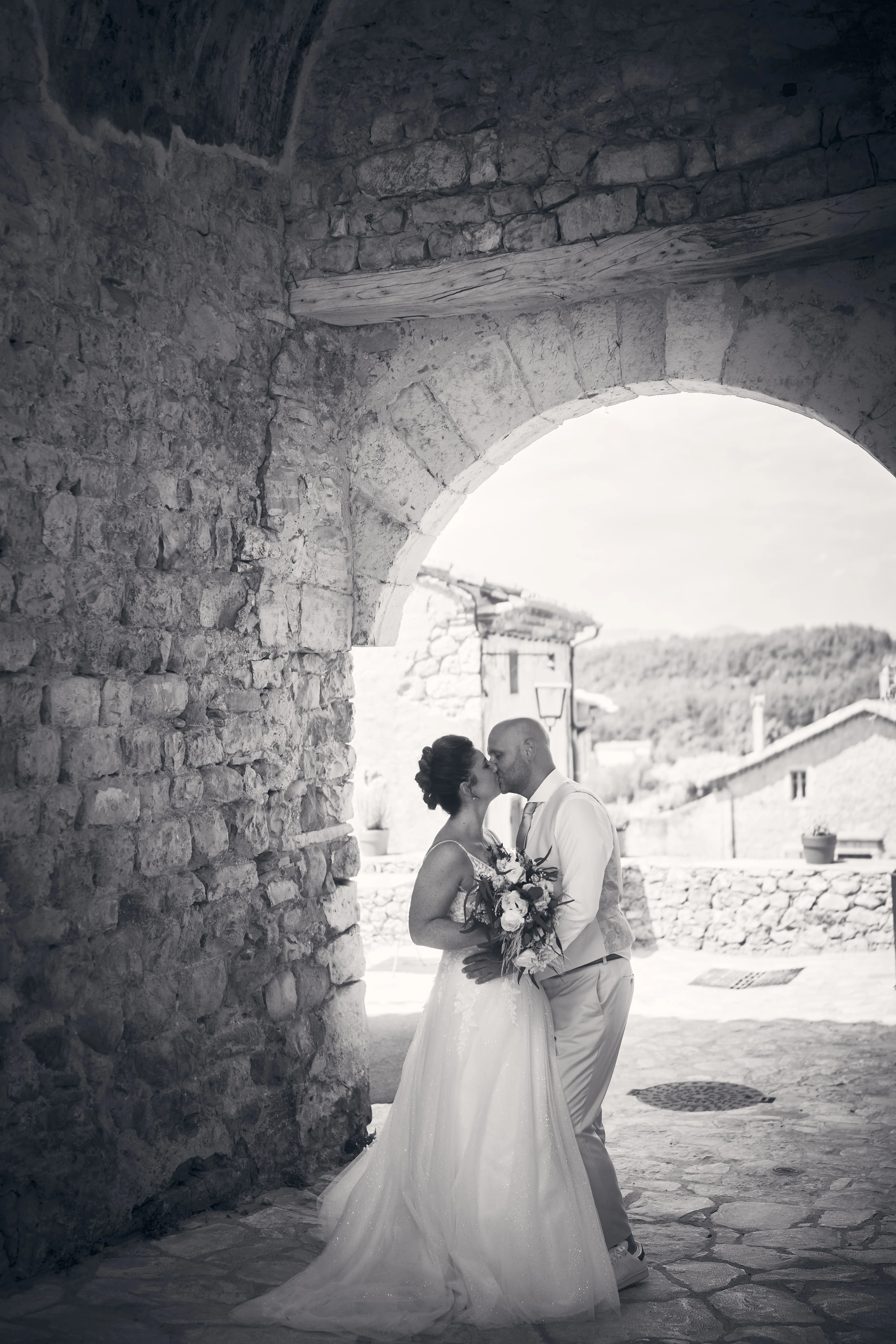 Portrait en noir et blanc des mariés sous une arche de pierre.