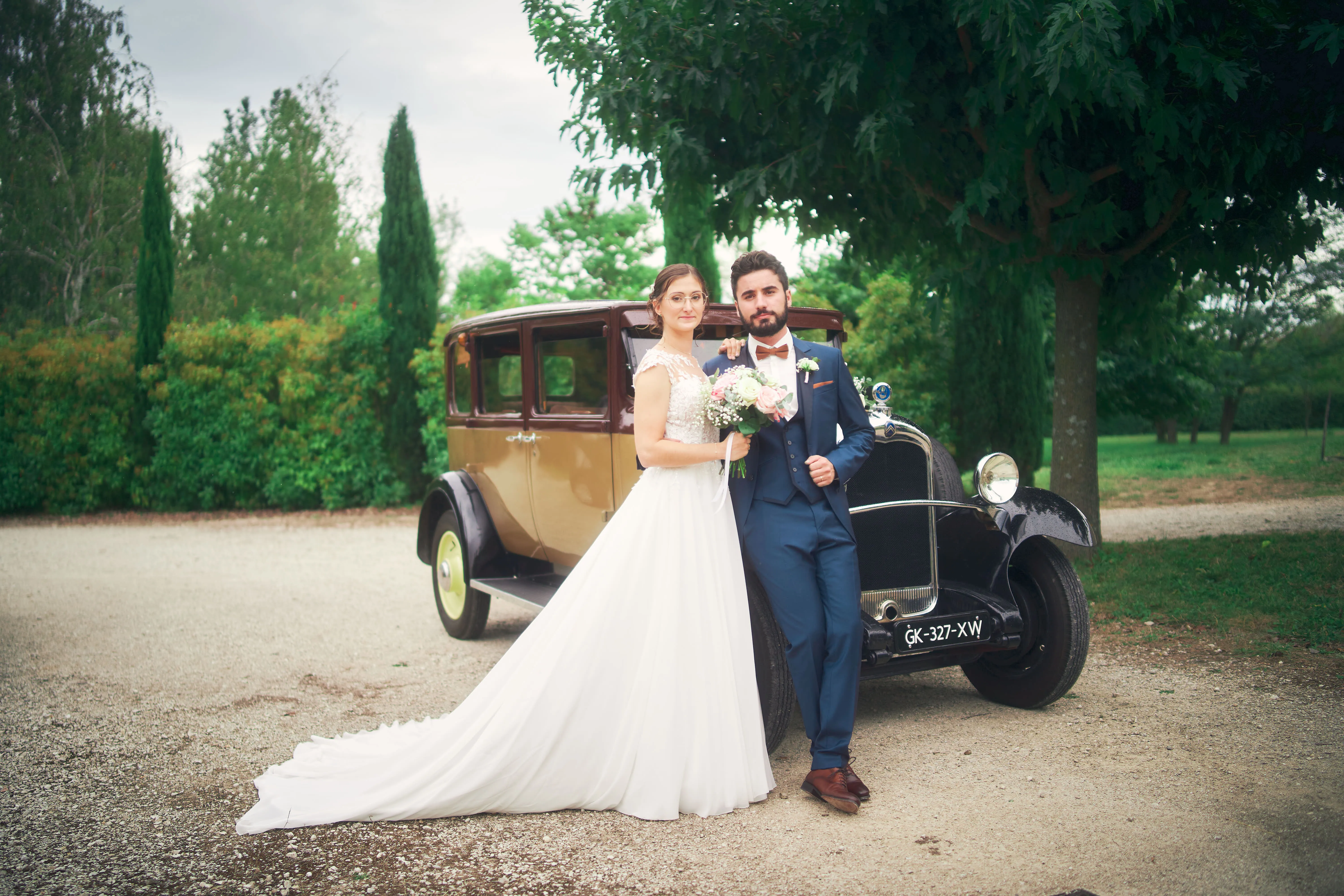 Couple de mariés devant une voiture ancienne dans un parc.