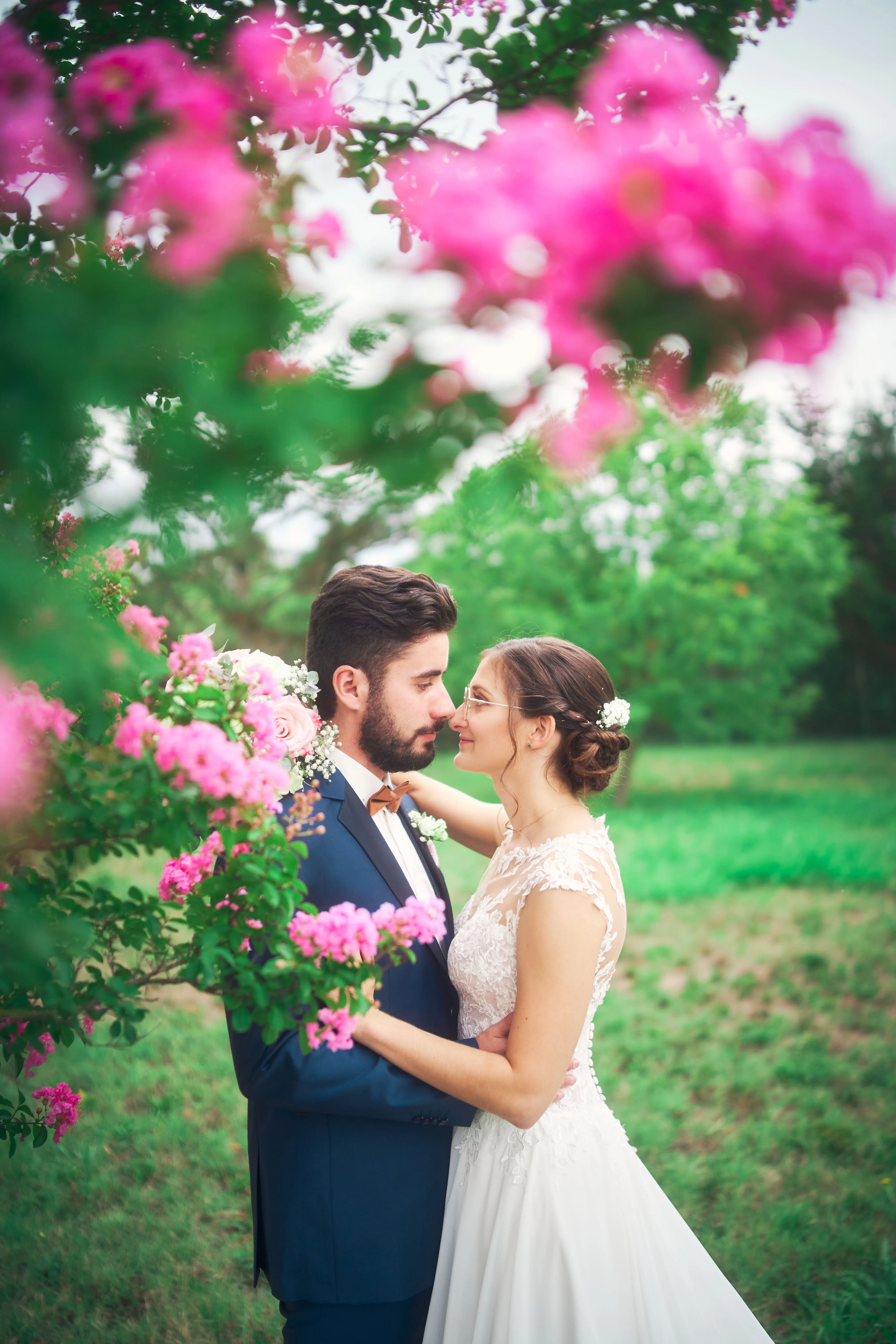 Mariés s'embrassant devant des fleurs roses.