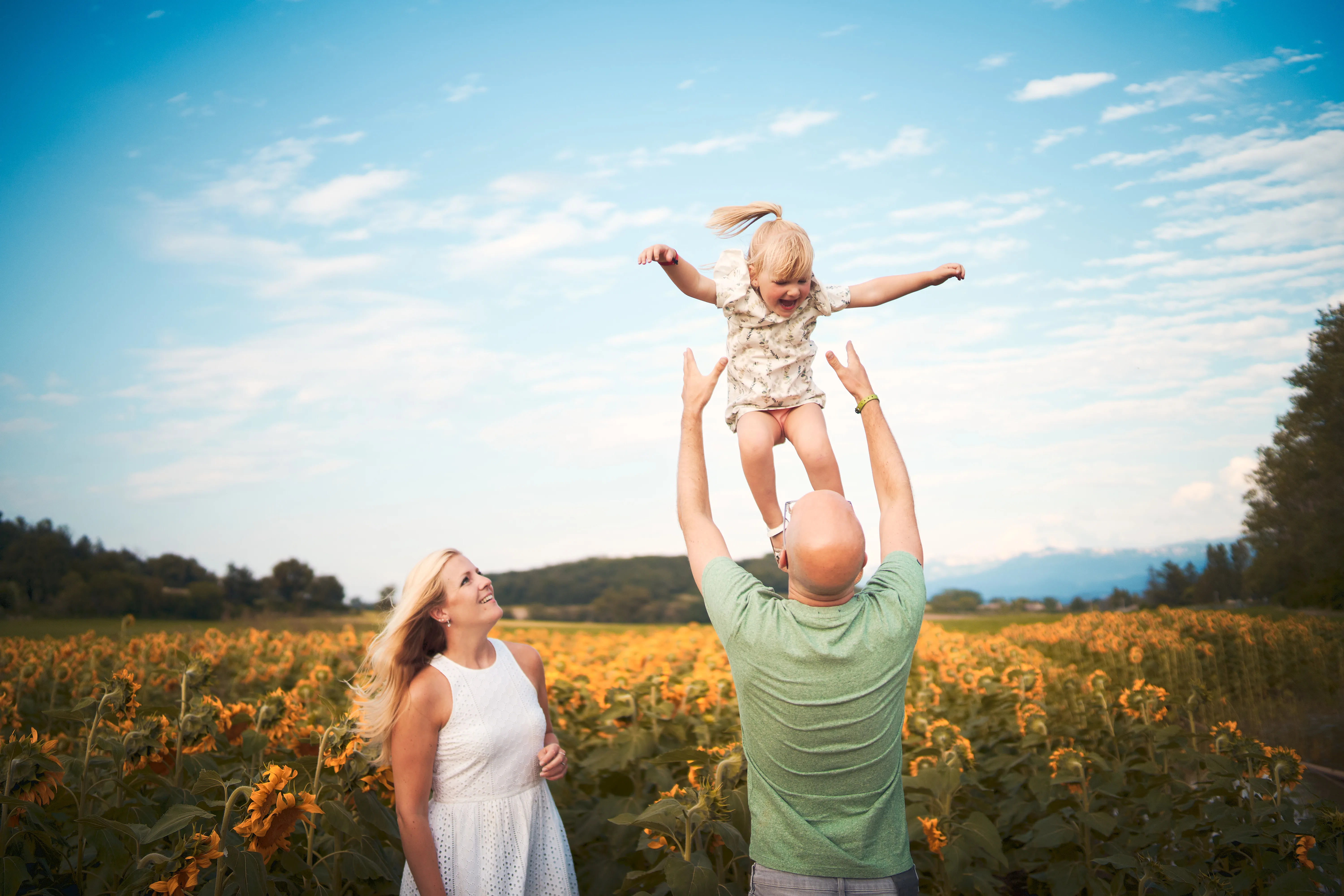 Père soulevant son enfant au milieu d'un champ de tournesols.
