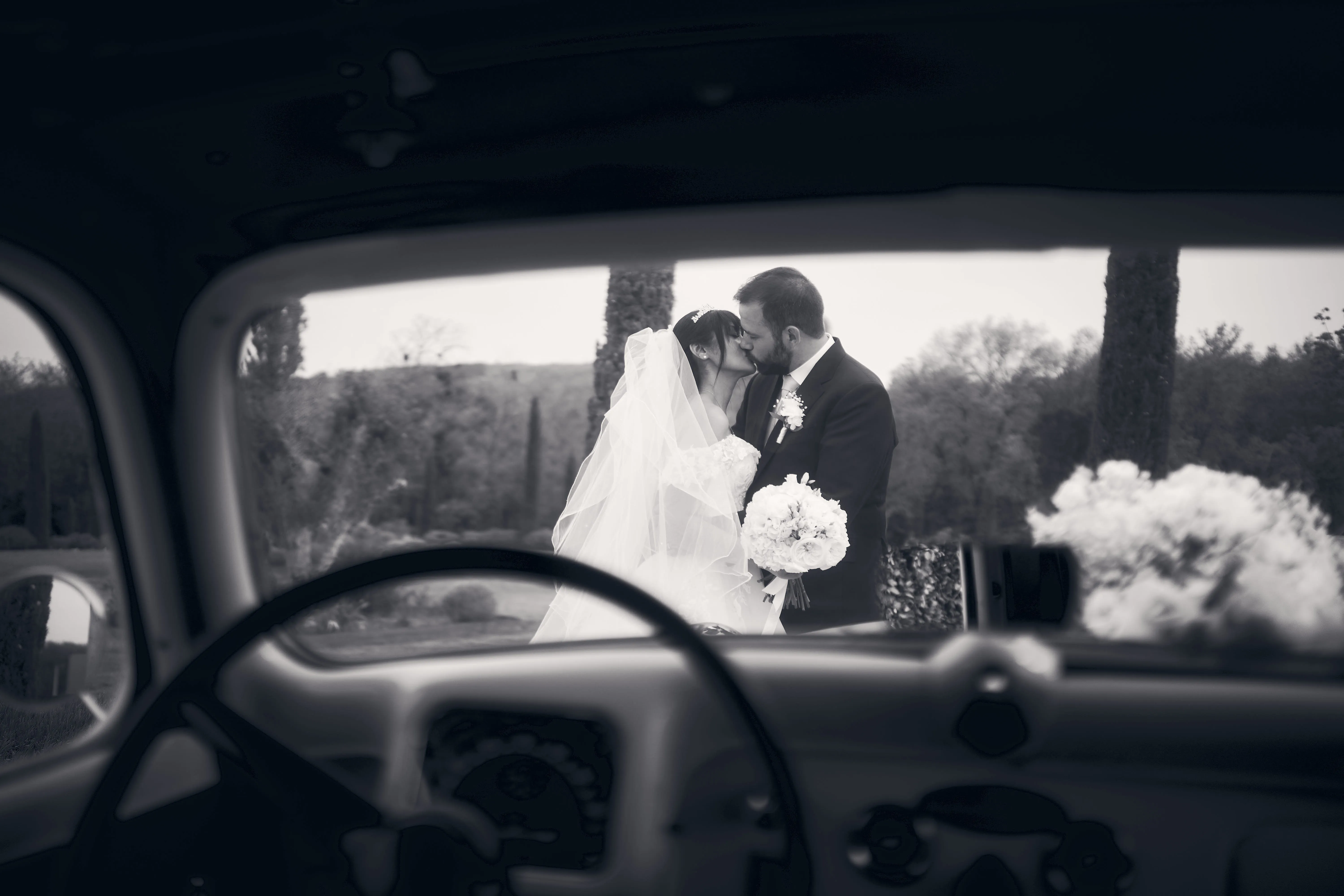Portrait en noir et blanc des mariés vu à travers une voiture.