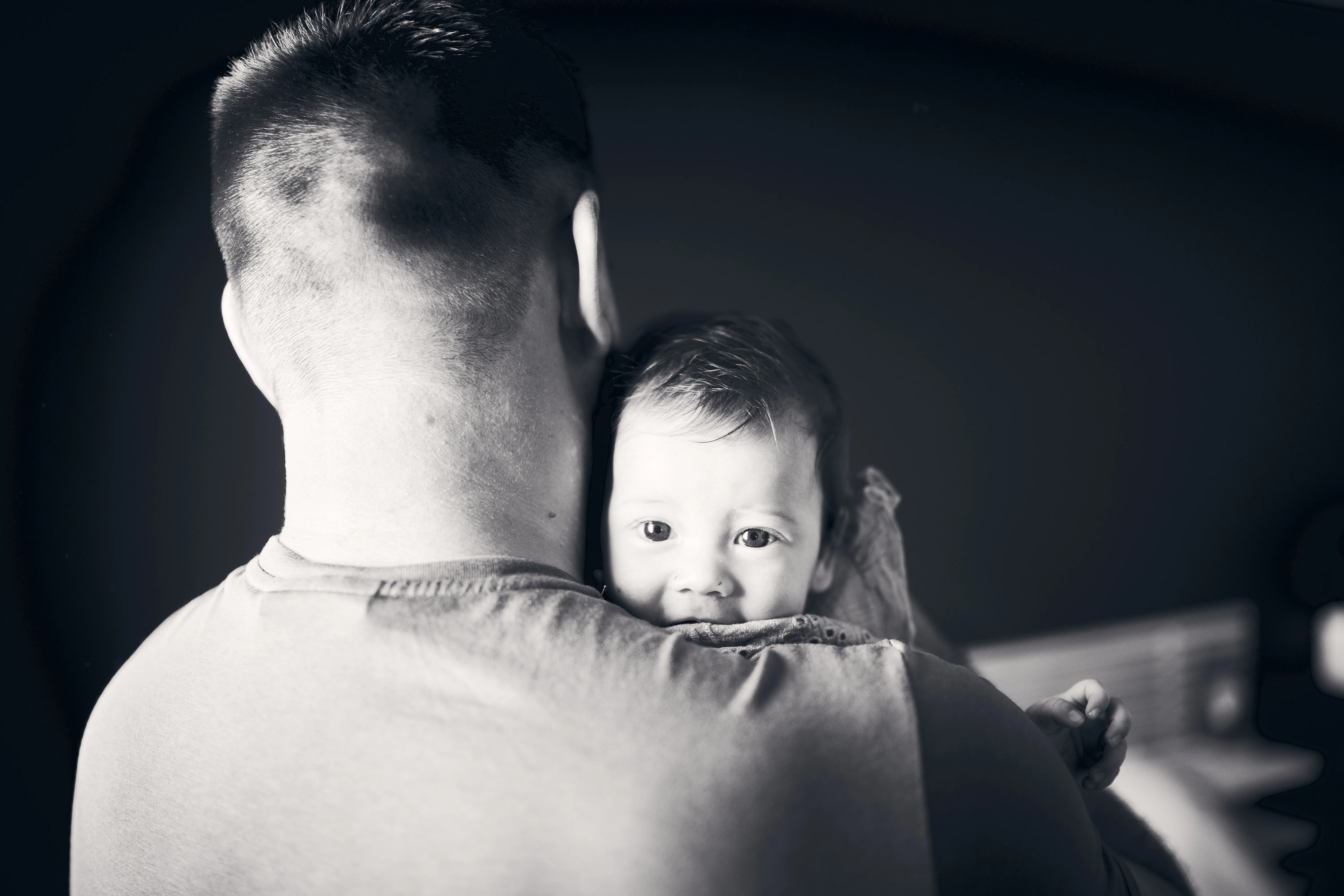 Bébé blotti contre l'épaule de son père en noir et blanc.