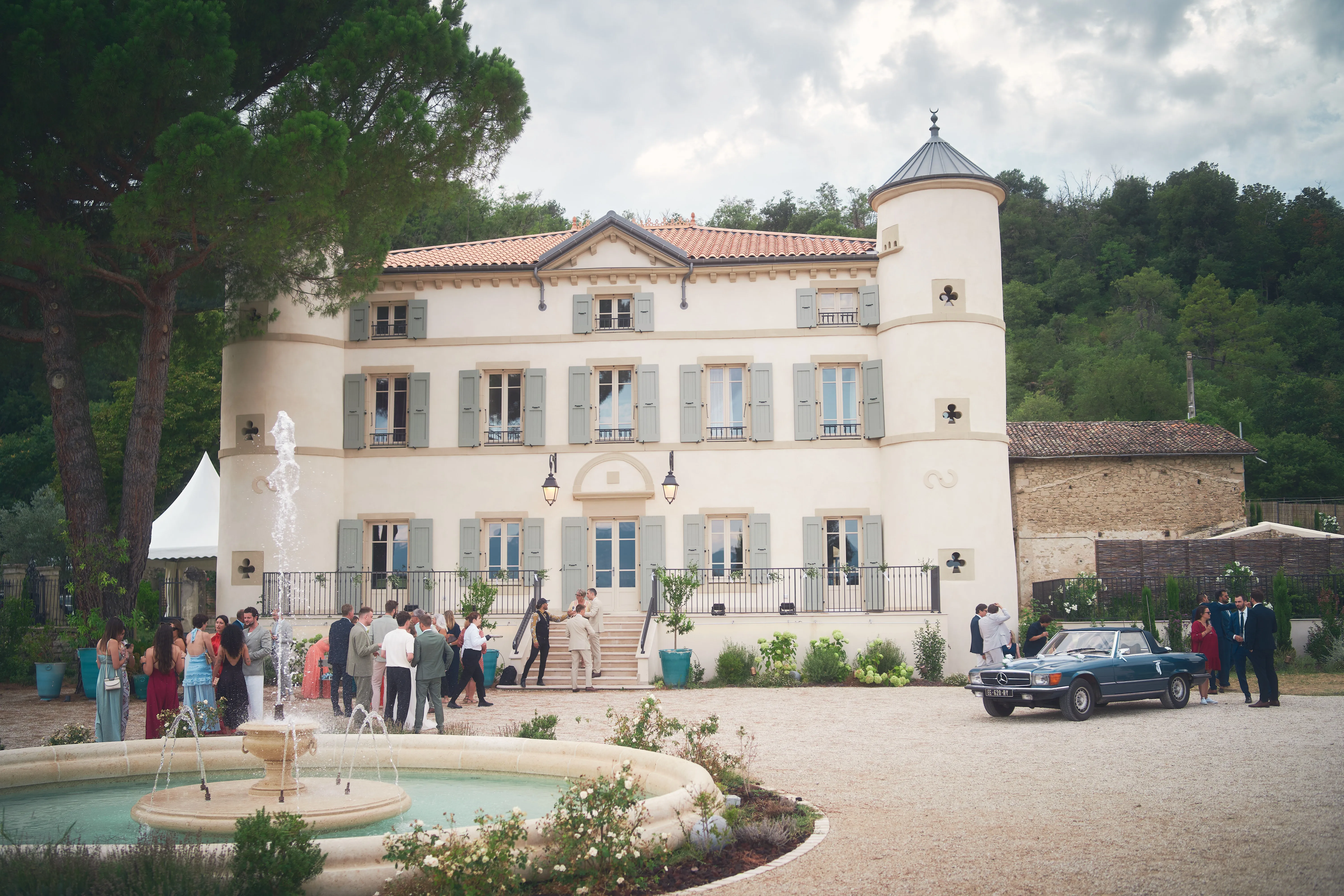 Invités devant une bâtisse de réception avec une fontaine au premier plan.