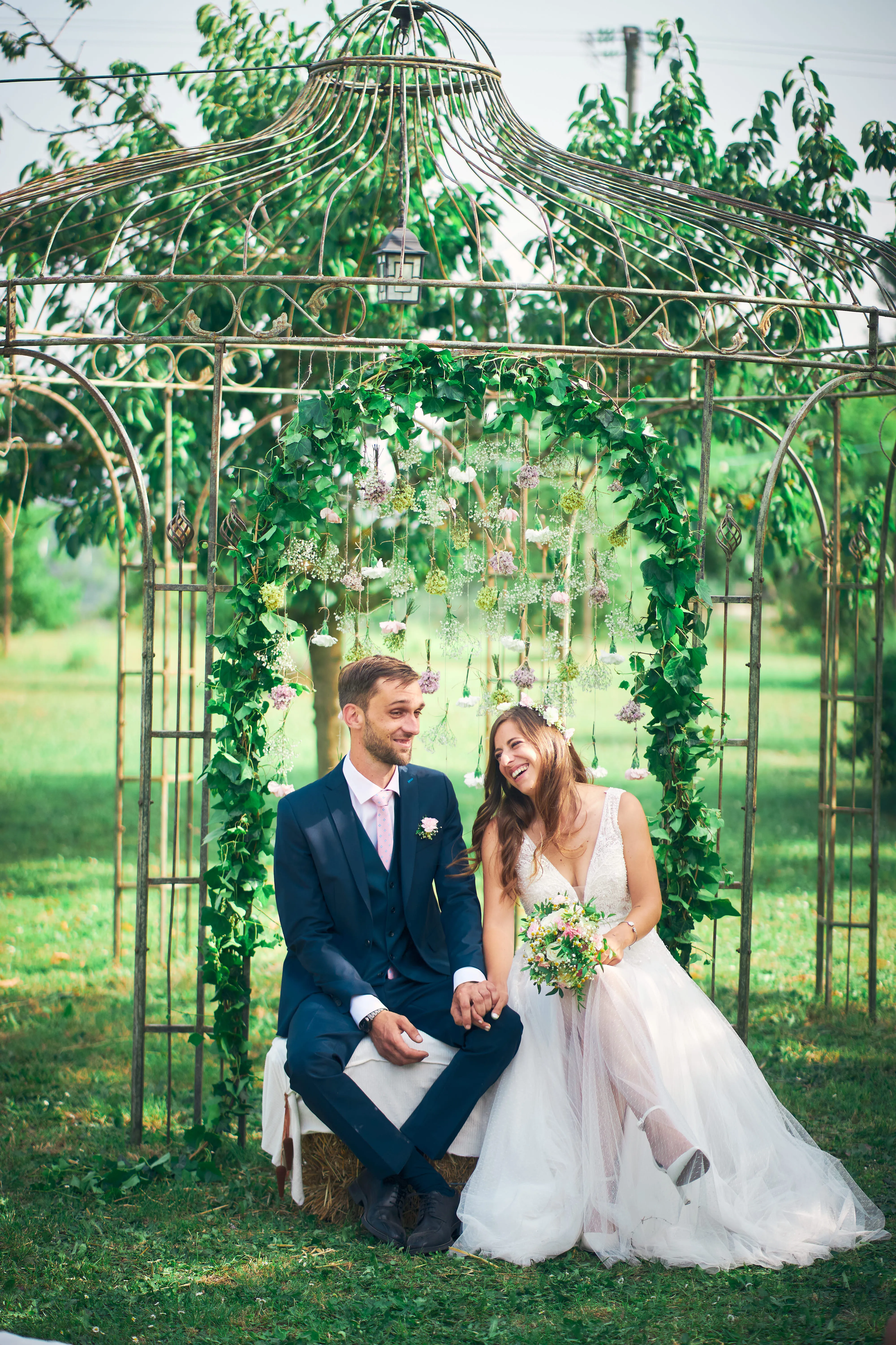 Couple de mariés assis sous une arche végétale.