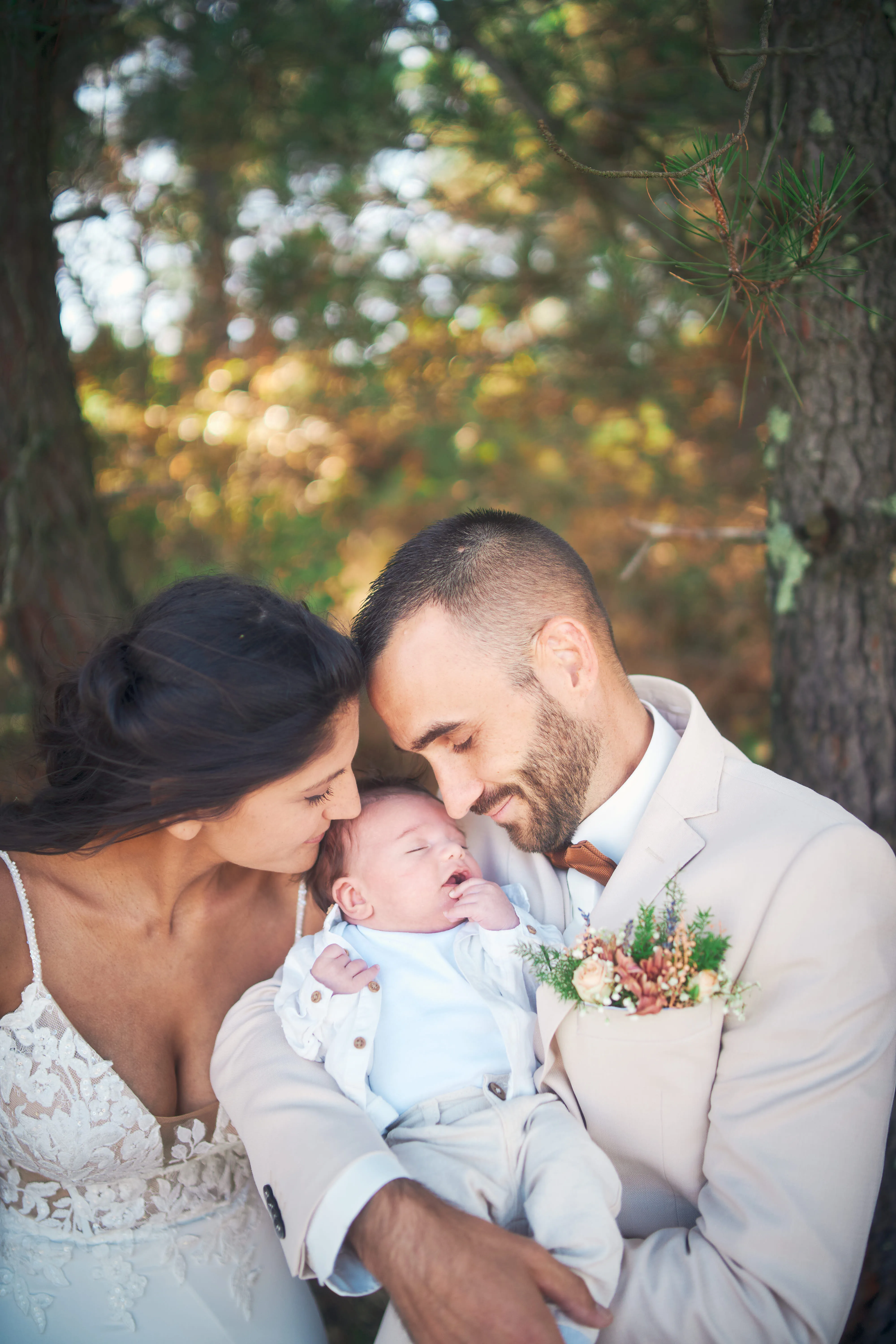 Mariés embrassant leur bébé sous les arbres.